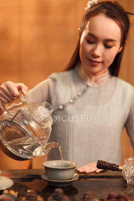 Schöne junge asiatische Frau gießt Wasser aus Wasserkocher in Tasse — Stockfoto