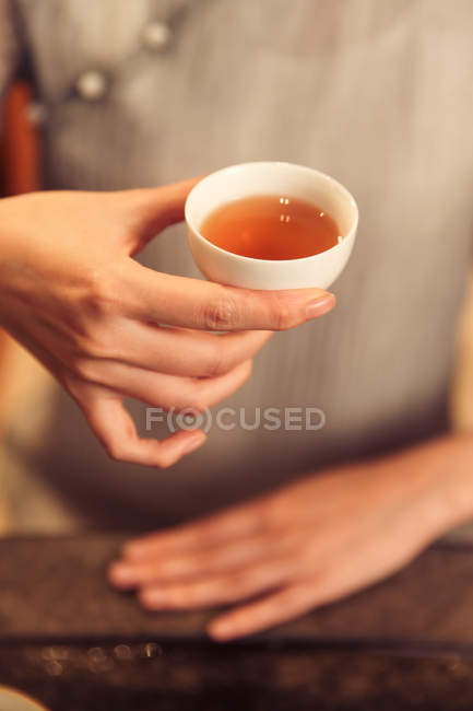 Tiro recortado de mujer sosteniendo taza blanca con té de hierbas aromáticas calientes - foto de stock