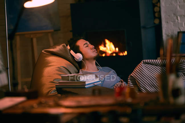Vista de cerca de las herramientas de arte y hombre joven en los auriculares sentados cerca de la chimenea, enfoque selectivo - foto de stock