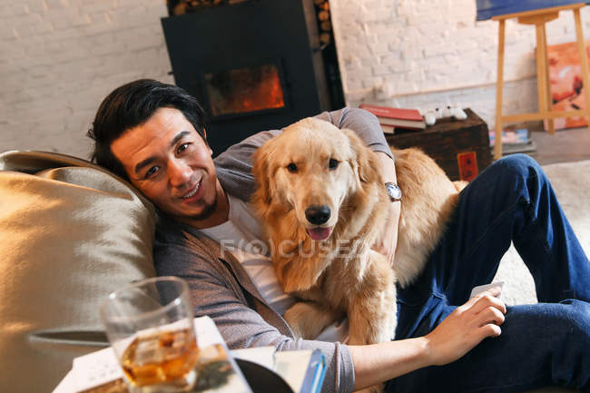 Blick aus der Vogelperspektive auf einen fröhlichen asiatischen Mann, der mit Hund auf einem Bohnensackstuhl ruht und zu Hause in die Kamera lächelt — Stockfoto