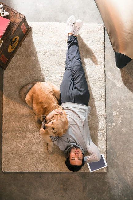 Vue de dessus de l'homme couché avec le chien sur le tapis et regardant la caméra — Photo de stock