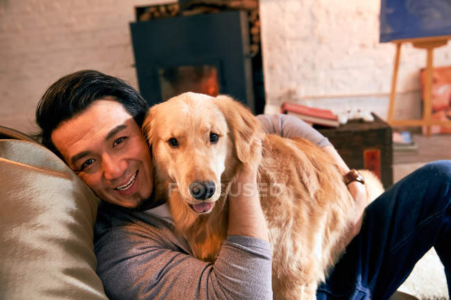 Feliz asiático homem abraçando cão e sorrindo para câmera em casa — Fotografia de Stock