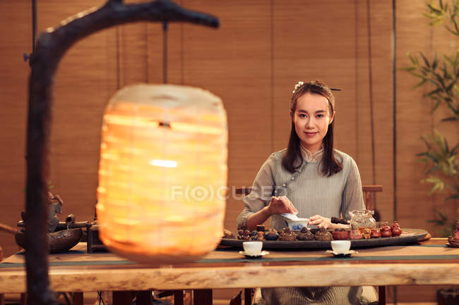 Close-up view of illuminated lantern on foreground and asian woman making tea and smiling at camera — Stock Photo