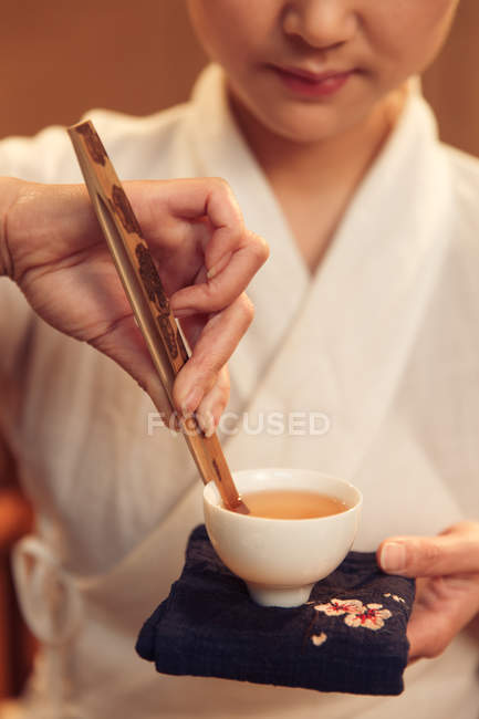 Cropped shot of young chinese woman holding white cup with hot organic herbal tea — Stock Photo