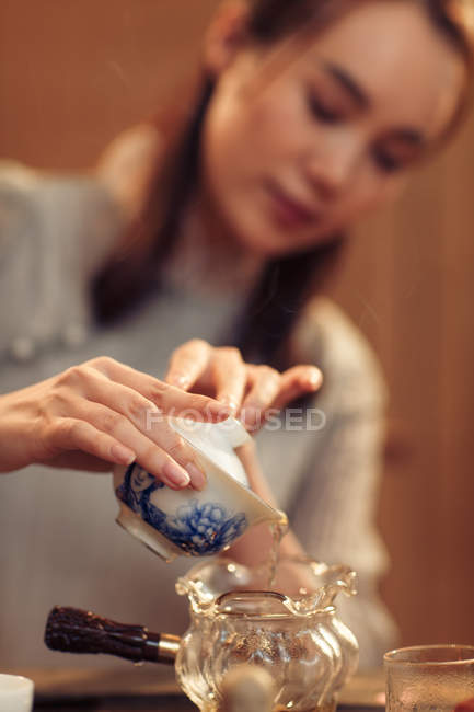 Tiro recortado de la mujer china enfocada vertiendo agua en el recipiente de vidrio, enfoque selectivo - foto de stock
