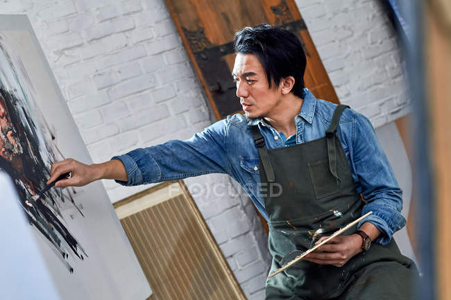 Selective focus of concentrated asian artist painting portrait in studio — Stock Photo