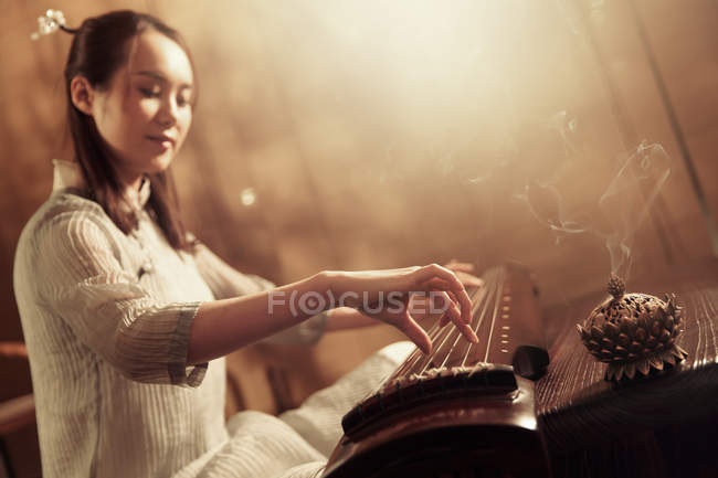 Bajo ángulo vista de joven asiático mujer jugando tradicional chino guzheng instrumento - foto de stock