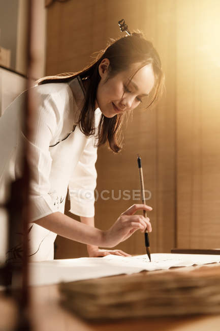 Souriant jeune asiatique femme tenant brosse et écriture chinois personnages — Photo de stock