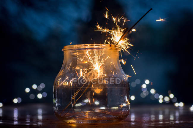 Vista close-up de frasco de vidro com brilhos em chamas no fundo festivo borrado — Fotografia de Stock