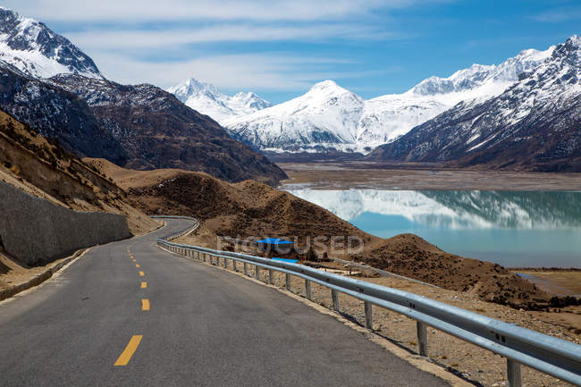 Camino vacío, montañas cubiertas de nieve y hermoso lago en el Tíbet - foto de stock