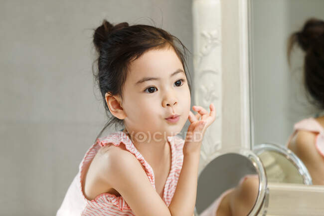 Menina aplicando creme em seu rosto na frente do espelho — Fotografia de Stock