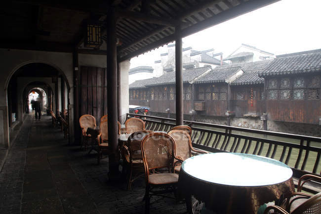 Столы со стульями на веранде, канале и домах в Хучжоу, Чжэцзян, Китай — стоковое фото