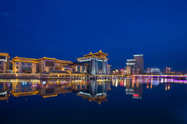 Edifícios iluminados refletidos em água calma à noite, deserto de Dunhuang, Gansu — Fotografia de Stock