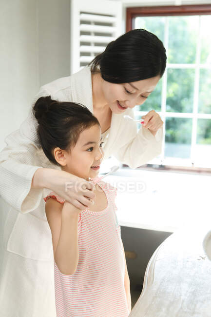 Madre enseñando hija cepillarse los dientes - foto de stock