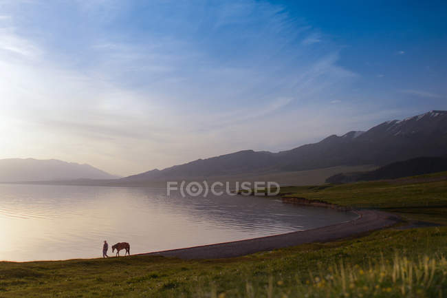 Hombre con caballo y paisaje del lago Sailimu de Xinjiang, China - foto de stock