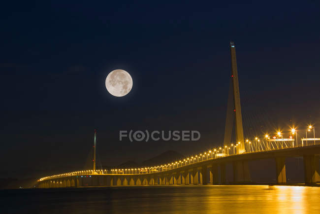 Puente iluminado y luna llena en el cielo nocturno, Shenzhen, China - foto de stock