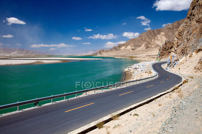 Camino de asfalto vacío, lago y montañas en el día soleado, Tíbet - foto de stock