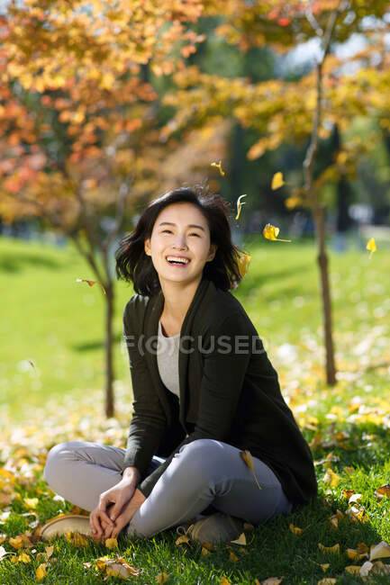 Jovem mulher sentada em folhas caídas na grama — Fotografia de Stock