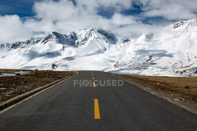 Пустая асфальтовая дорога и красивые заснеженные горы в Тибете — стоковое фото