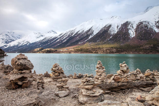 Красивый пейзаж с заснеженными горами и сложенными камнями на берегу озера — стоковое фото
