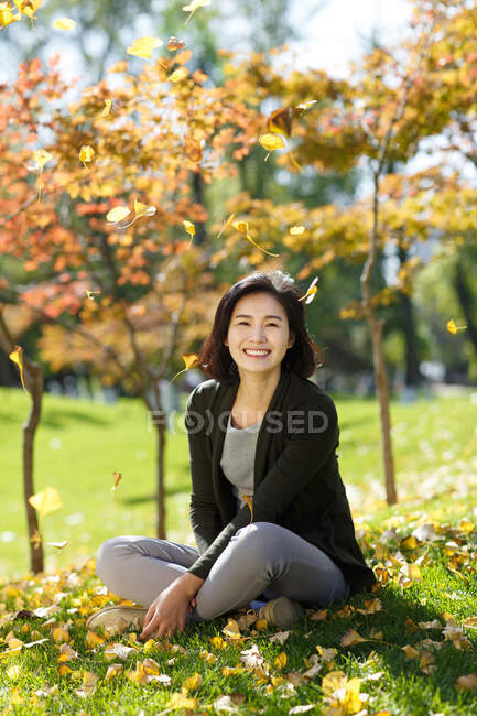 Mujer joven sentada sobre hojas caídas en hierba - foto de stock