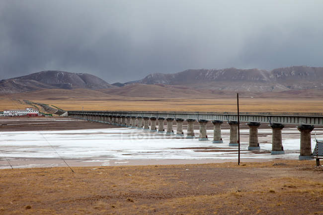 Ponte sul fiume e montagne panoramiche al giorno nuvoloso, Hoh Xil, Qinghai — Foto stock