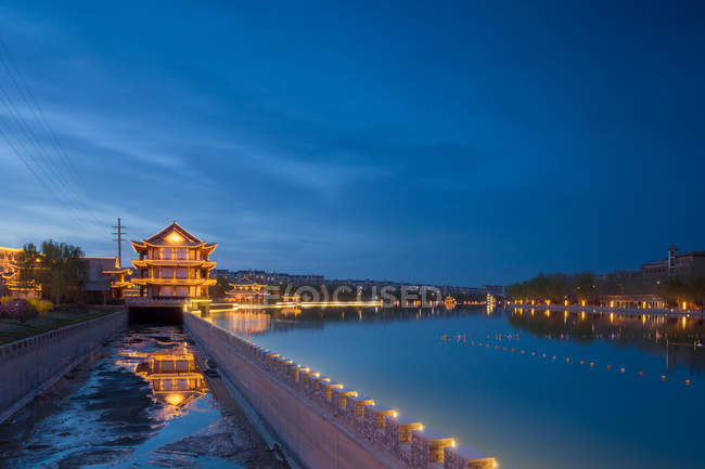 Освещенные здания и спокойная вода ночью, пустыня Дуньхуан, Ганьсу — стоковое фото