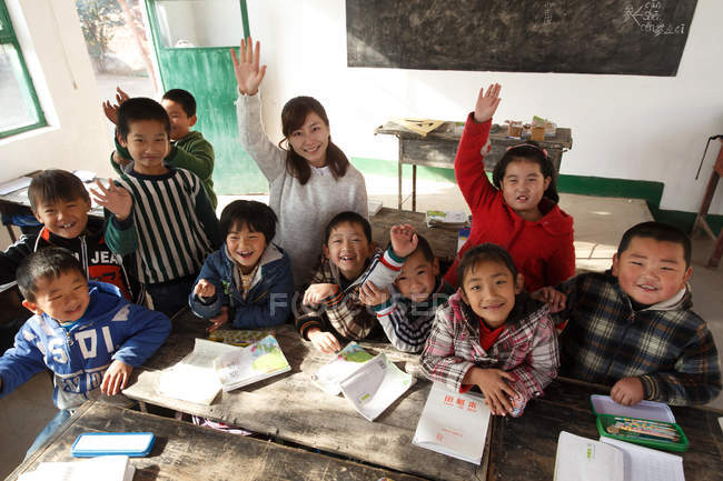 Aus der Vogelperspektive: Lehrerin und chinesische Schüler heben die Hände und lächeln in die Kamera im Klassenzimmer — Stockfoto