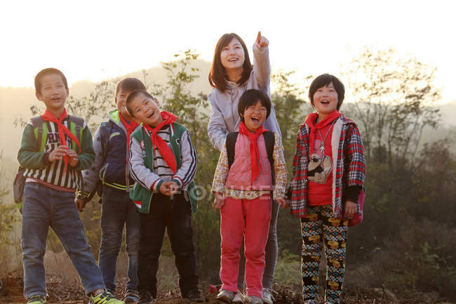 Rural female teacher pointing with finger for chinese students standing outdoor — Stock Photo