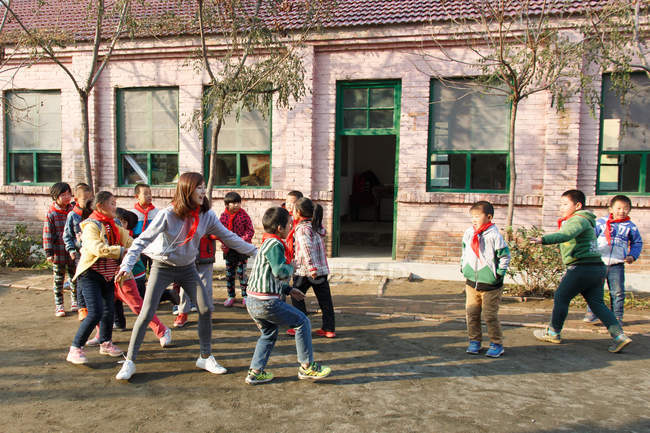 Insegnante donna rurale e alunni felici che giocano insieme nel cortile della scuola — Foto stock