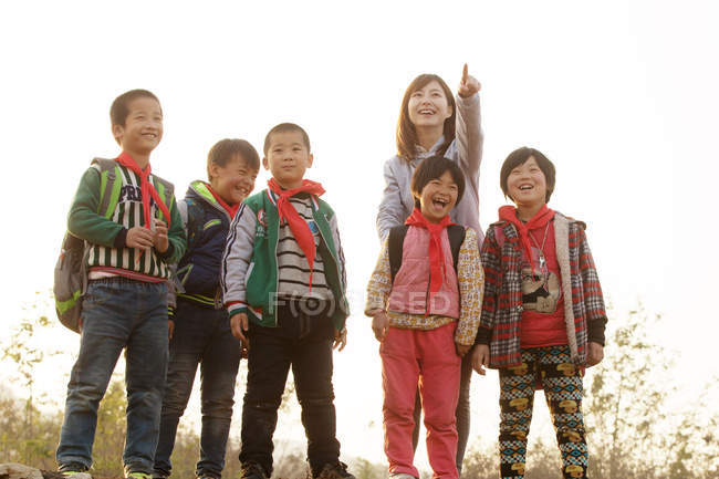 Rural female teacher pointing with finger for chinese students standing outdoor — Stock Photo