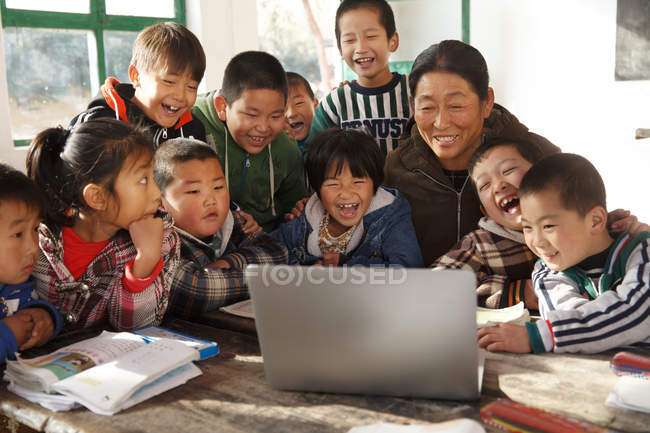 Professora rural e alunos usando computador portátil juntas na escola — Fotografia de Stock