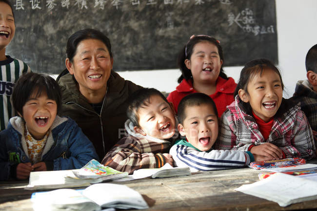 Profesora rural y alumnas chinas riendo en el aula - foto de stock