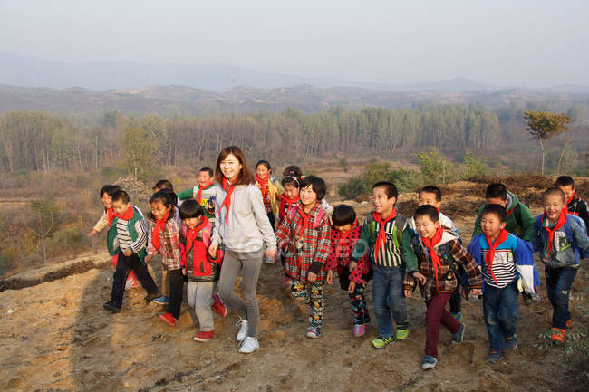 Young female teacher and chinese school students playing in rural area — Stock Photo