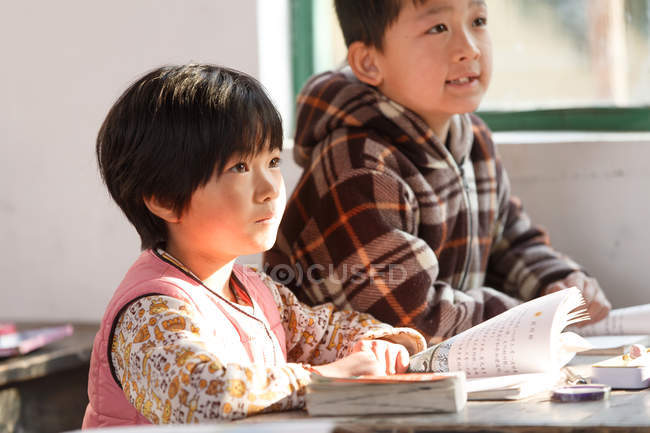 Estudiantes chinos de primaria sentados en el escritorio de la escuela rural - foto de stock