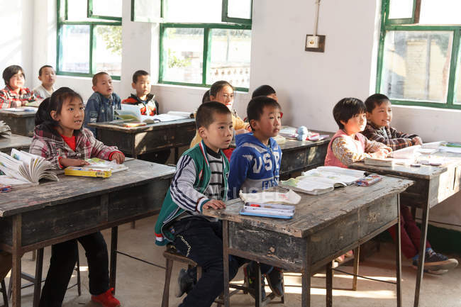 Estudiantes chinos sentados en escritorios y estudiando en la escuela primaria rural - foto de stock