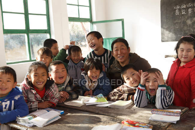 Rural female teacher and happy chinese pupils smiling at camera in the classroom — Stock Photo