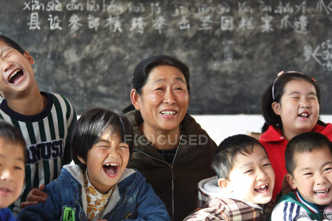 Rural female teacher and happy chinese pupils in classroom — Stock Photo