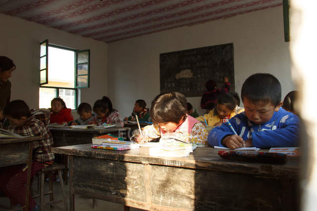 Estudiantes de primaria sentados y escribiendo en la escuela primaria rural - foto de stock