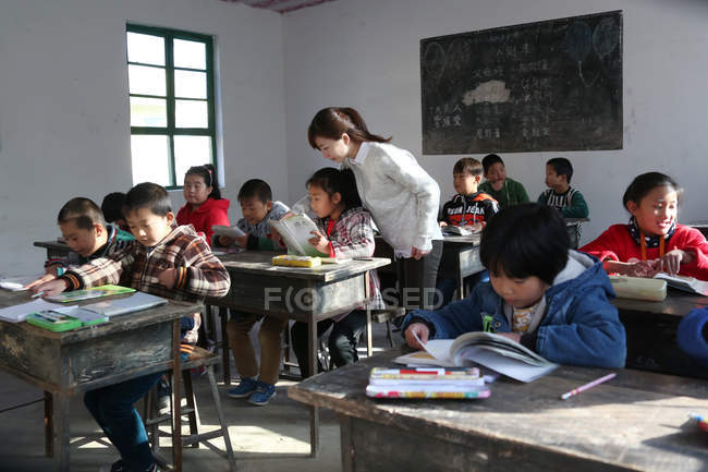 Rural female teacher looking at pupils studying in classroom — Stock Photo