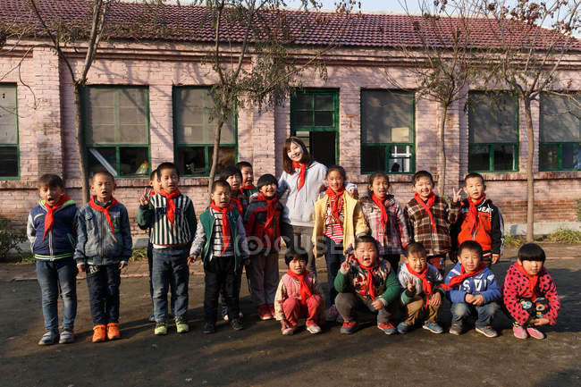 Profesora rural y alumnas chinas felices de pie juntas en el patio de la escuela - foto de stock