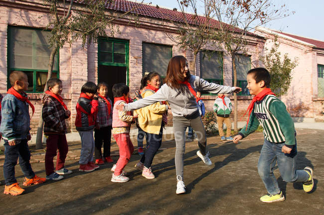Profesora rural y alumnas felices jugando juntas en el patio de la escuela - foto de stock