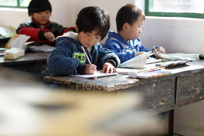 Estudiantes de primaria sentados en escritorios de la escuela primaria rural, enfoque selectivo - foto de stock