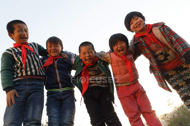 Vista basso angolo di felici alunni cinesi in piedi insieme e sorridente alla fotocamera esterna — Foto stock