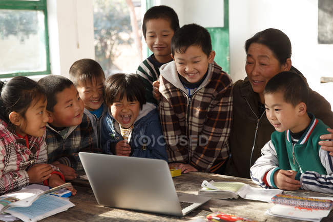 Professora rural e alunos usando computador portátil juntas na escola — Fotografia de Stock