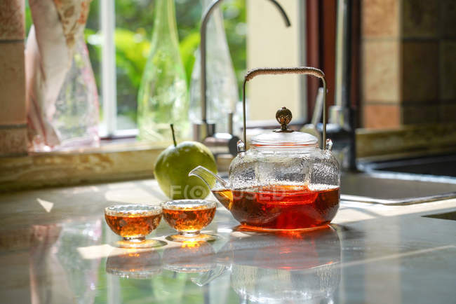 Vista de primer plano del juego de té de vidrio con hervidor de agua y vasos de vidrio en la mesa - foto de stock