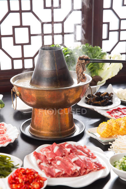 Крупный план горячей бараньей кастрюли, палочки для еды с мясом и вкусные ингредиенты на столе — стоковое фото