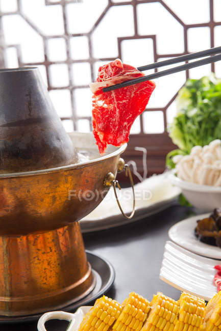 Vista de cerca de la olla caliente de cordero, palillos con carne e ingredientes deliciosos en la mesa - foto de stock