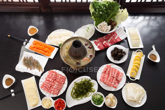 Vista en ángulo alto de la olla caliente de cordero con deliciosos ingredientes en la mesa - foto de stock