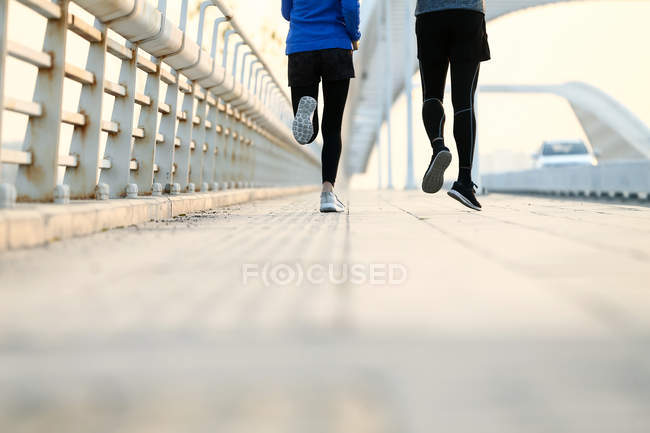 Plan recadré de jeune couple sportif courant ensemble sur le pont — Photo de stock